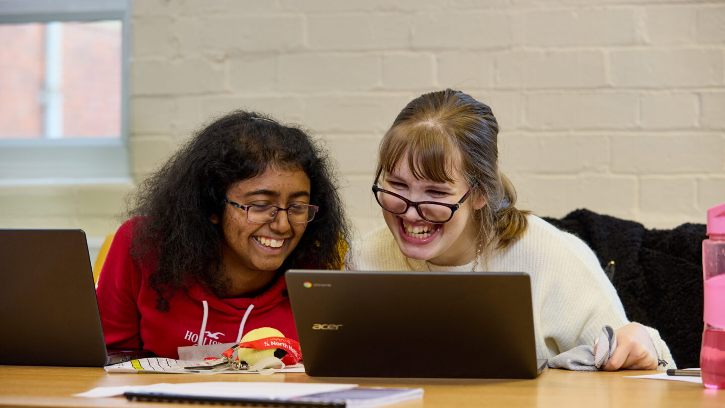 Photo of two students laughing and working together on laptops