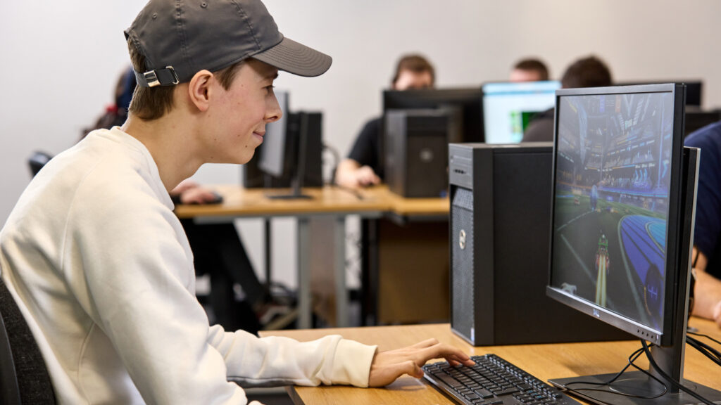 Photo of a student sat at a desk in a classroom playing a computer game